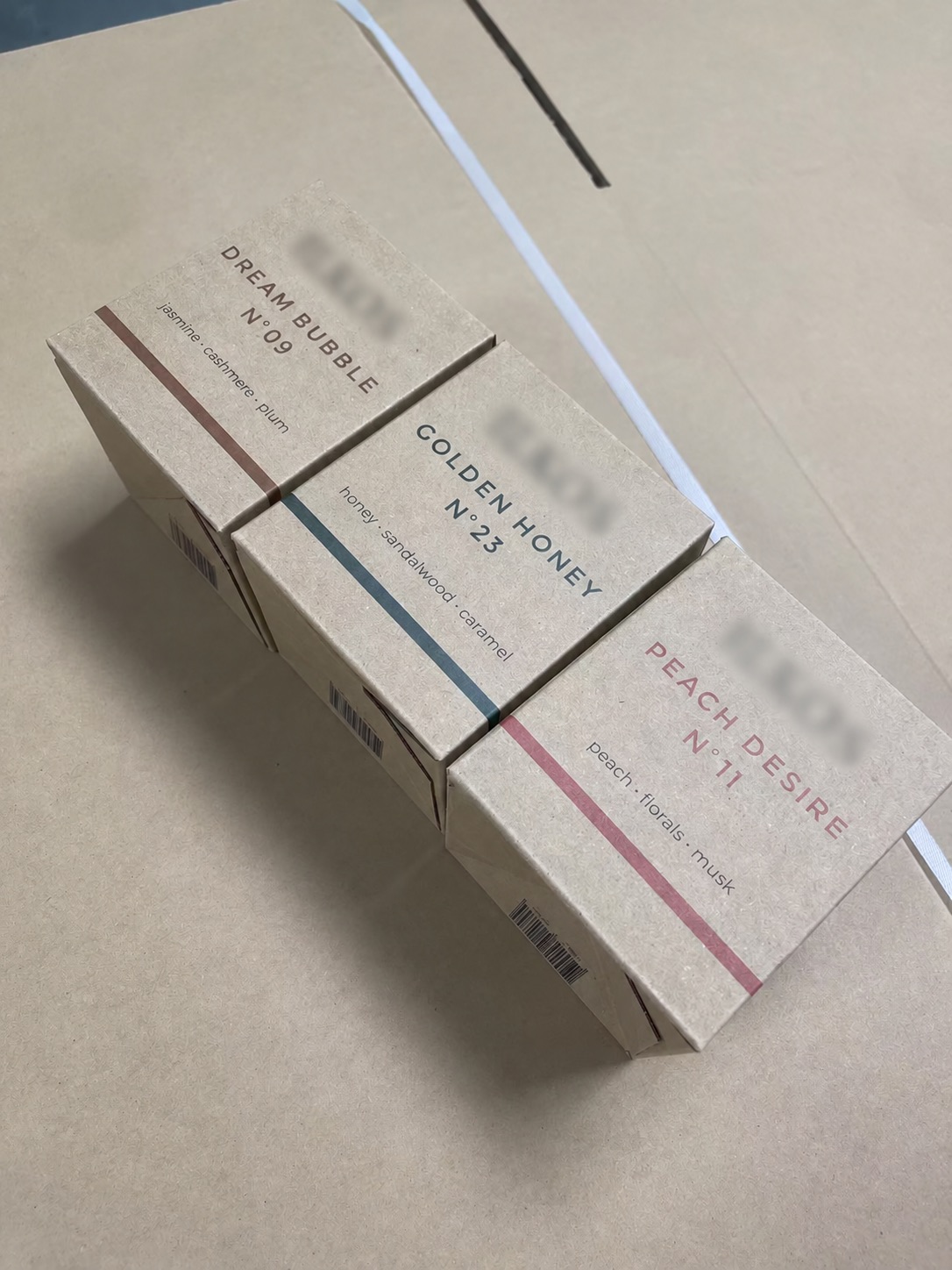Four candle carton variants in different fragrance colours, with customer branding blurred